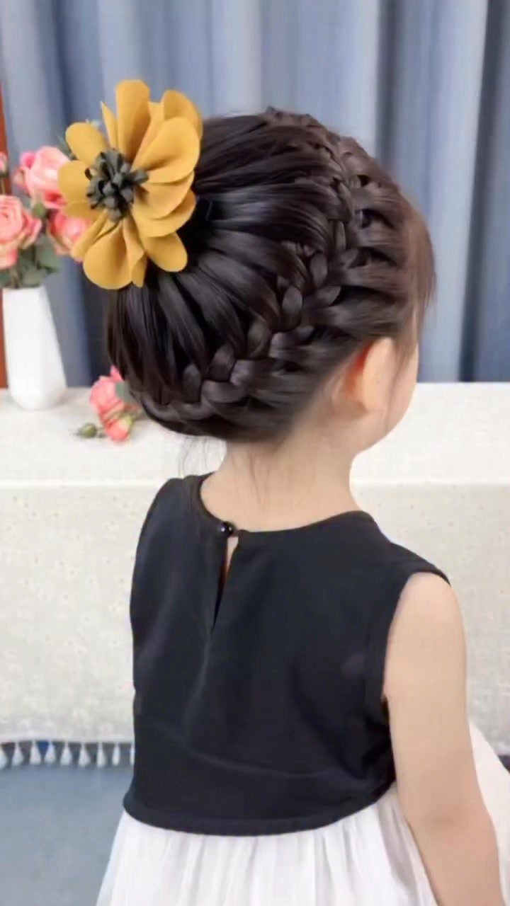 Young girl with a complex braided and twisted updo and yellow flower accessory.