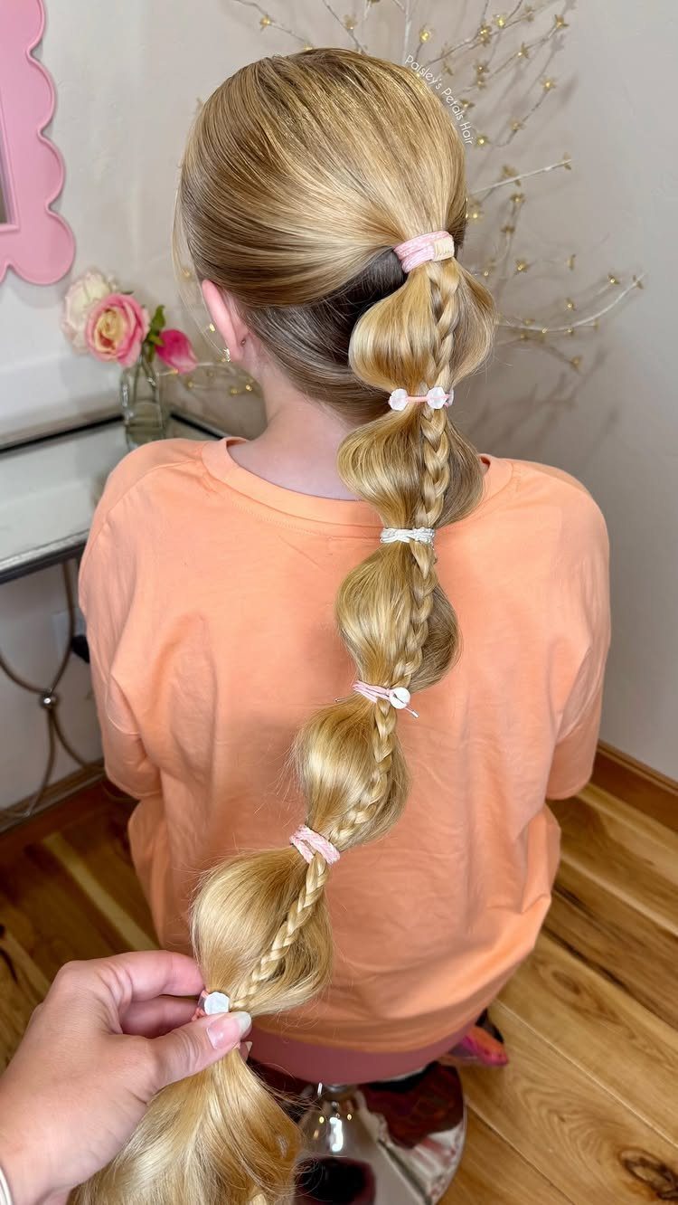 Blonde child's hair styled in a long bubble braid with pink elastic bands.