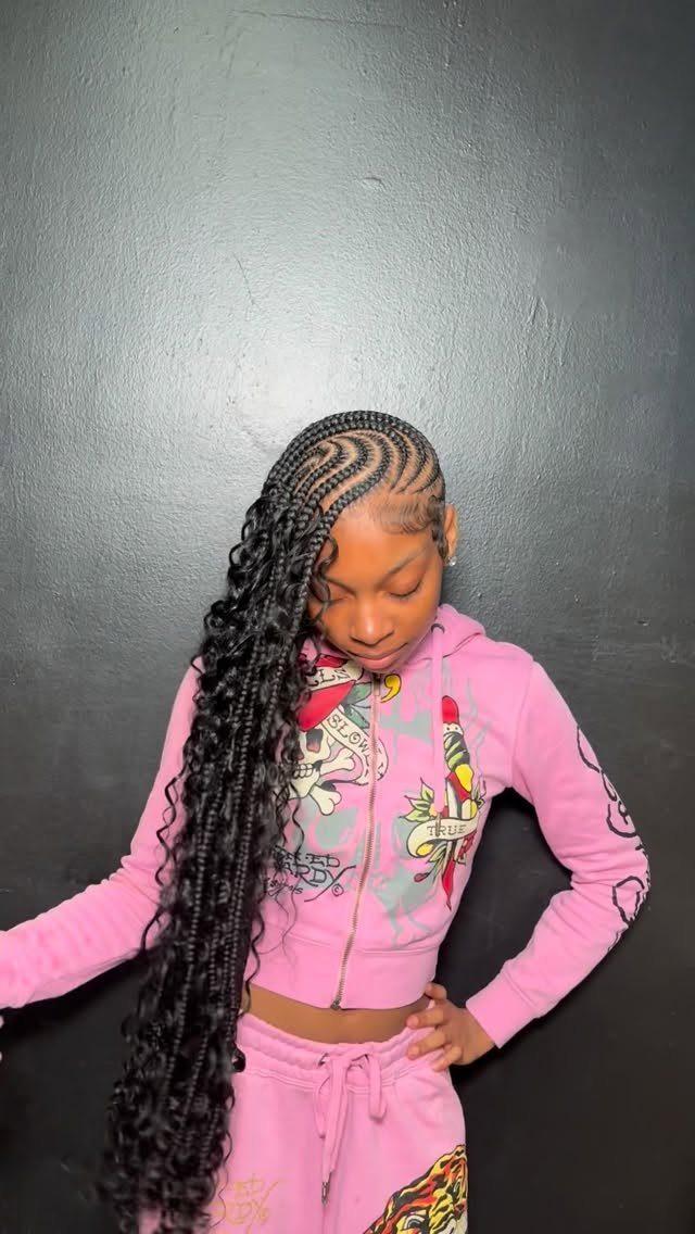 Young girl with long black braided cornrows wearing a pink tracksuit against dark wall