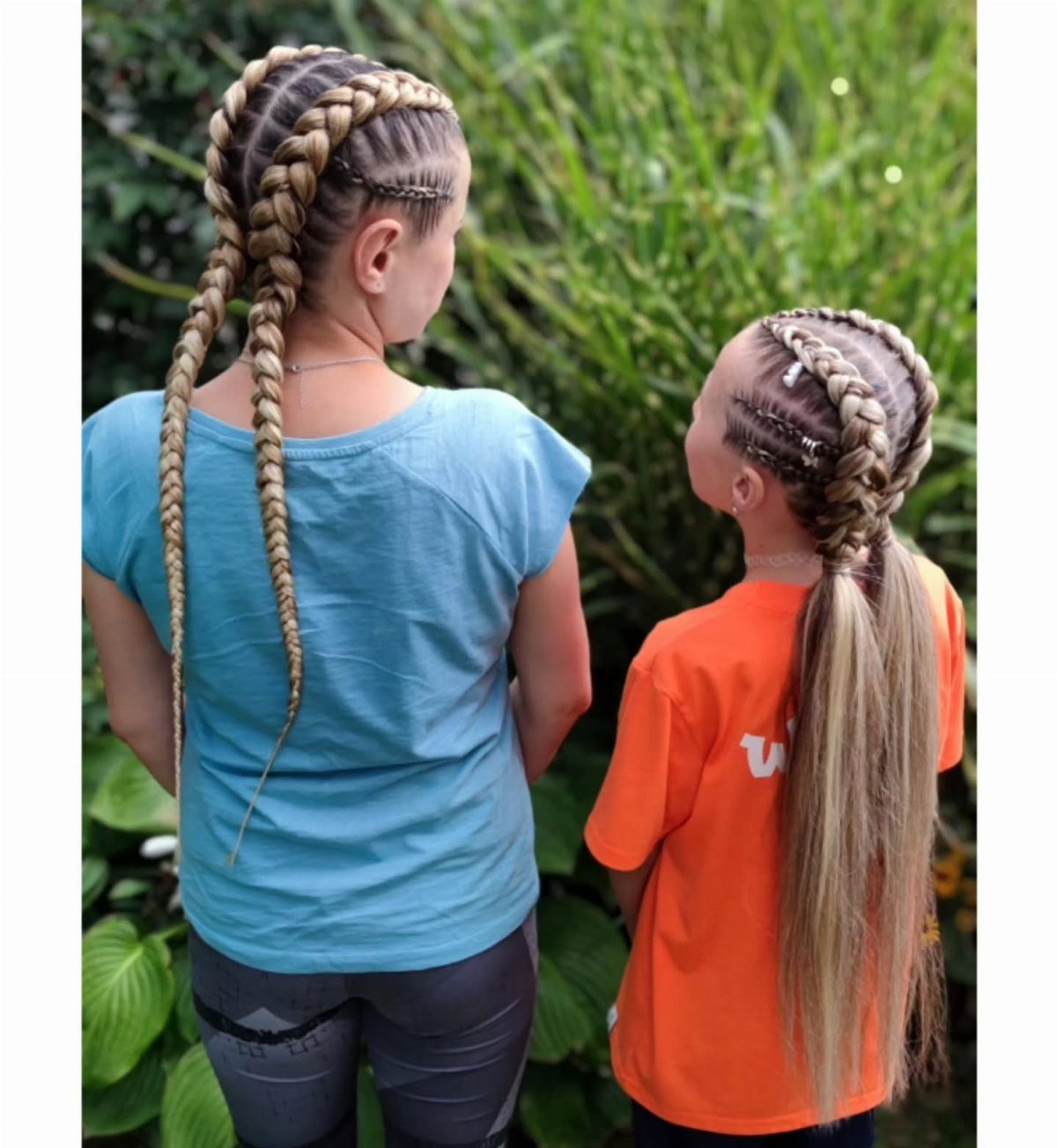 Woman and girl with blonde double Dutch braids standing in a green garden