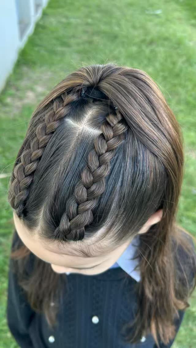 Two Dutch braids on a child's brown hair tied with a black band.