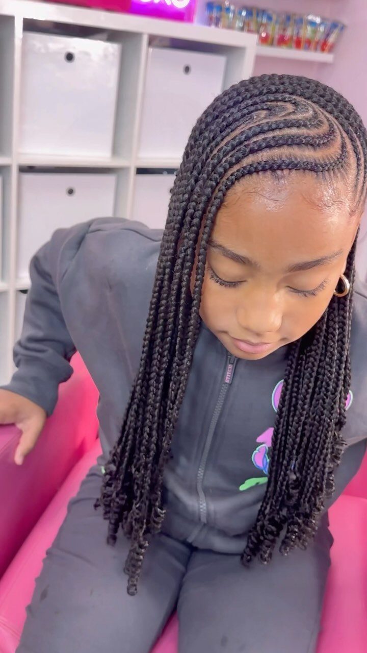 Young girl with side-swept lemonade braids wearing a grey tracksuit in a room.