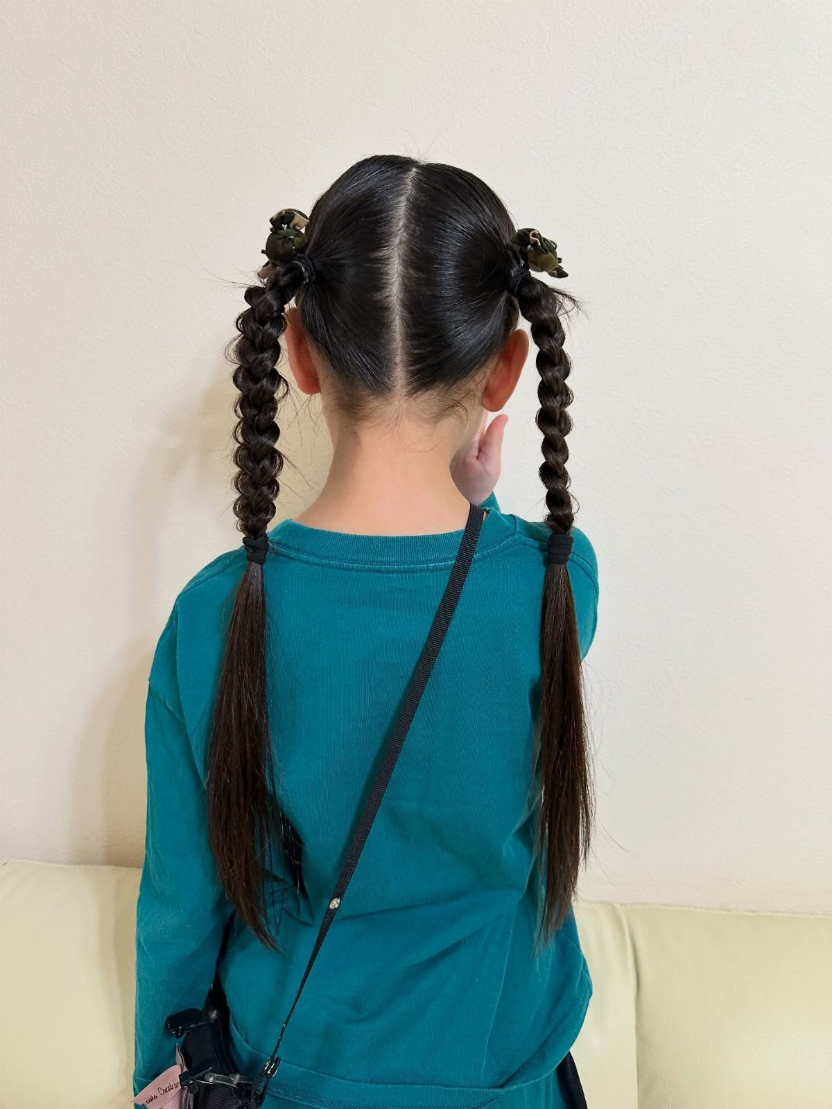 Child with dark hair styled in two braided pigtails wearing a teal shirt.