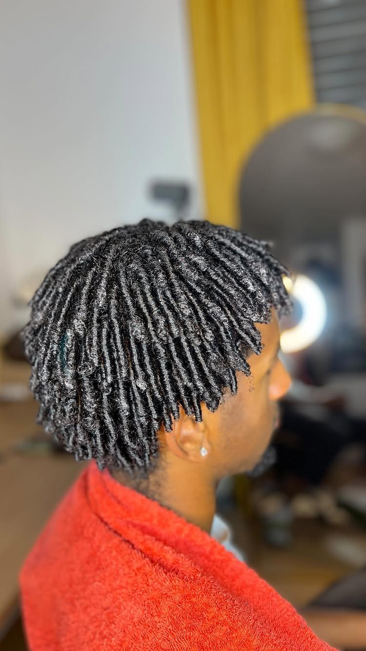 Man with short black two-strand twist braids wearing a red towel around shoulders.