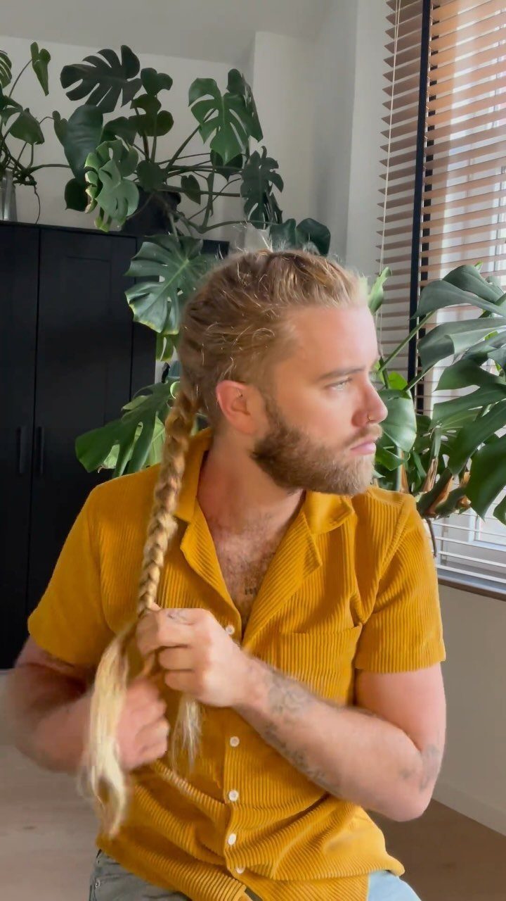 Blonde man with a beard wearing a yellow shirt and a long braid.