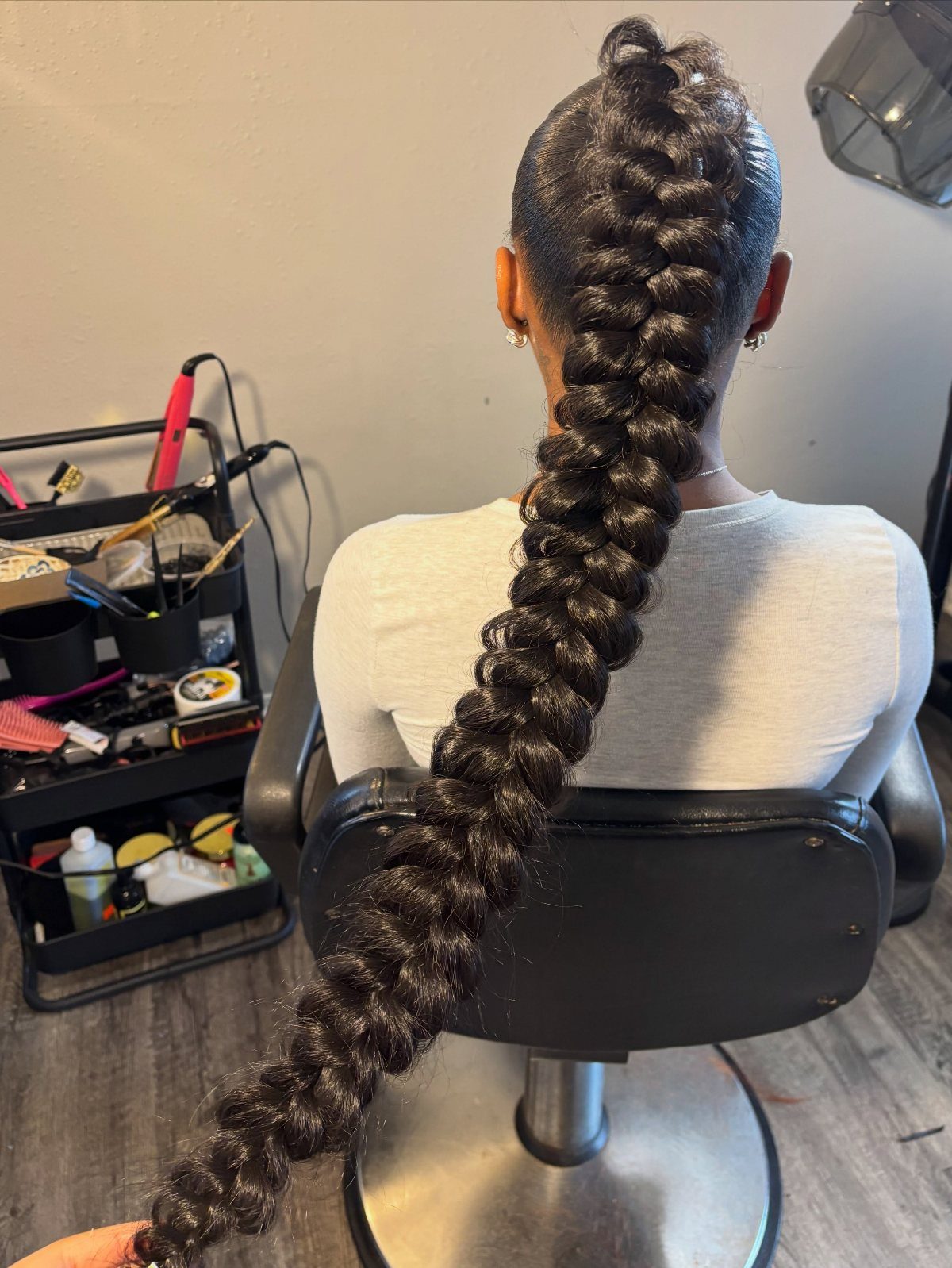 Long dark braided ponytail extending down the back of a person in white.