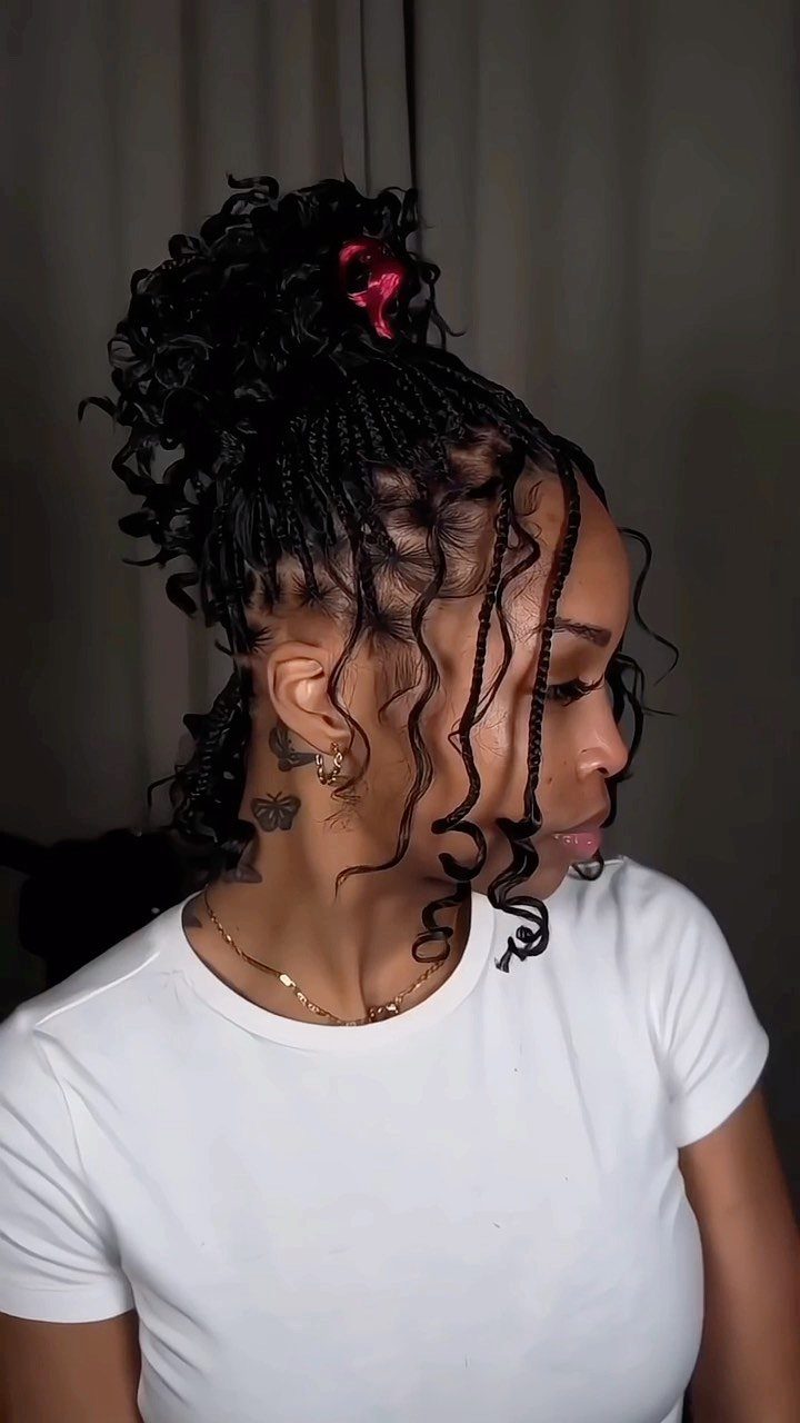 Woman with black braided hair styled in a high curly bun and tendrils.