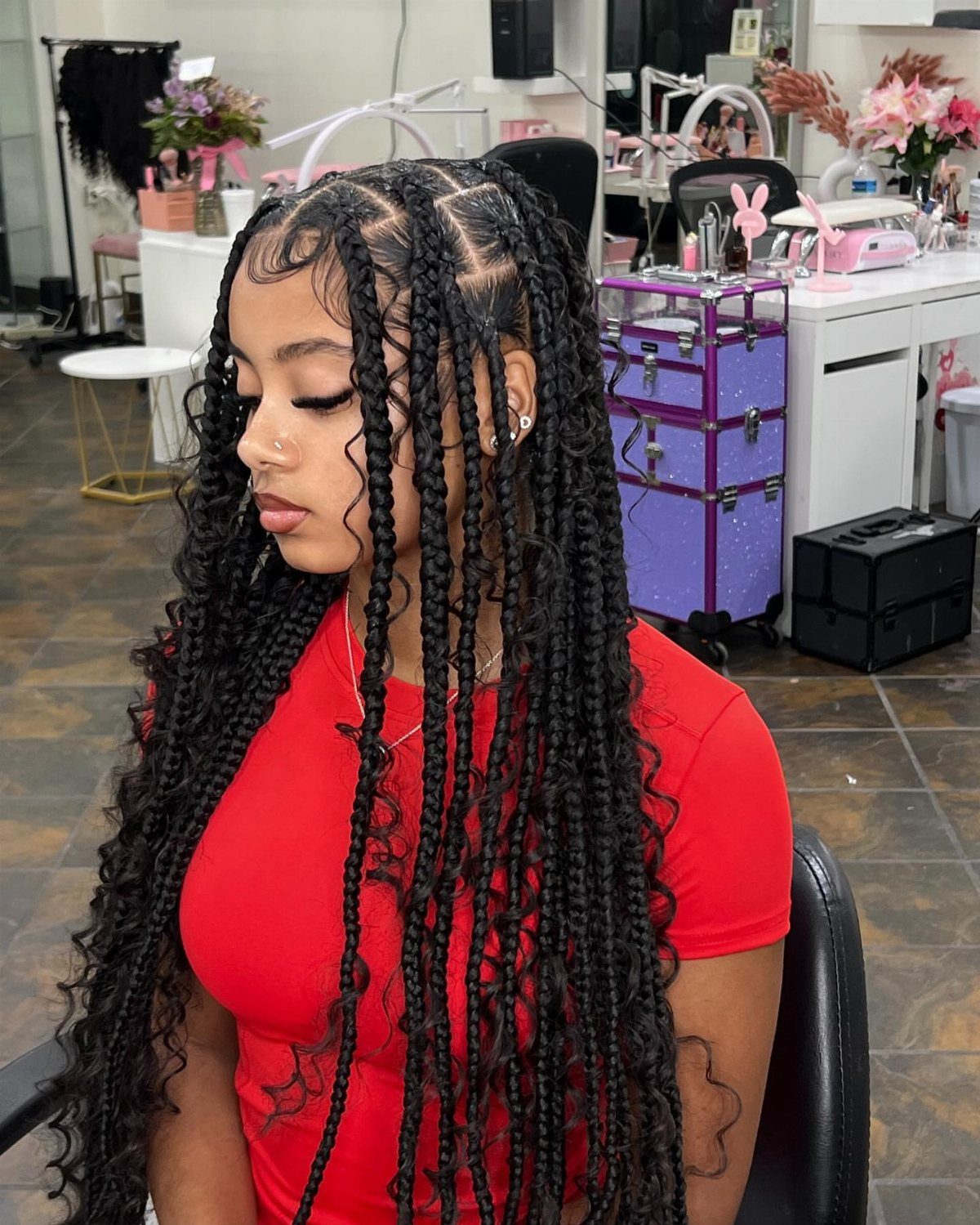 Woman with long curly feed-in braids wearing a red shirt in a salon