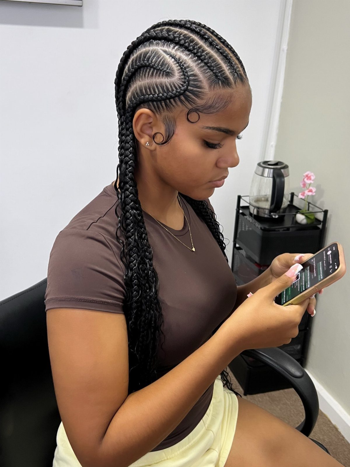 Woman with curved cornrow braids looking at her smartphone in a room.