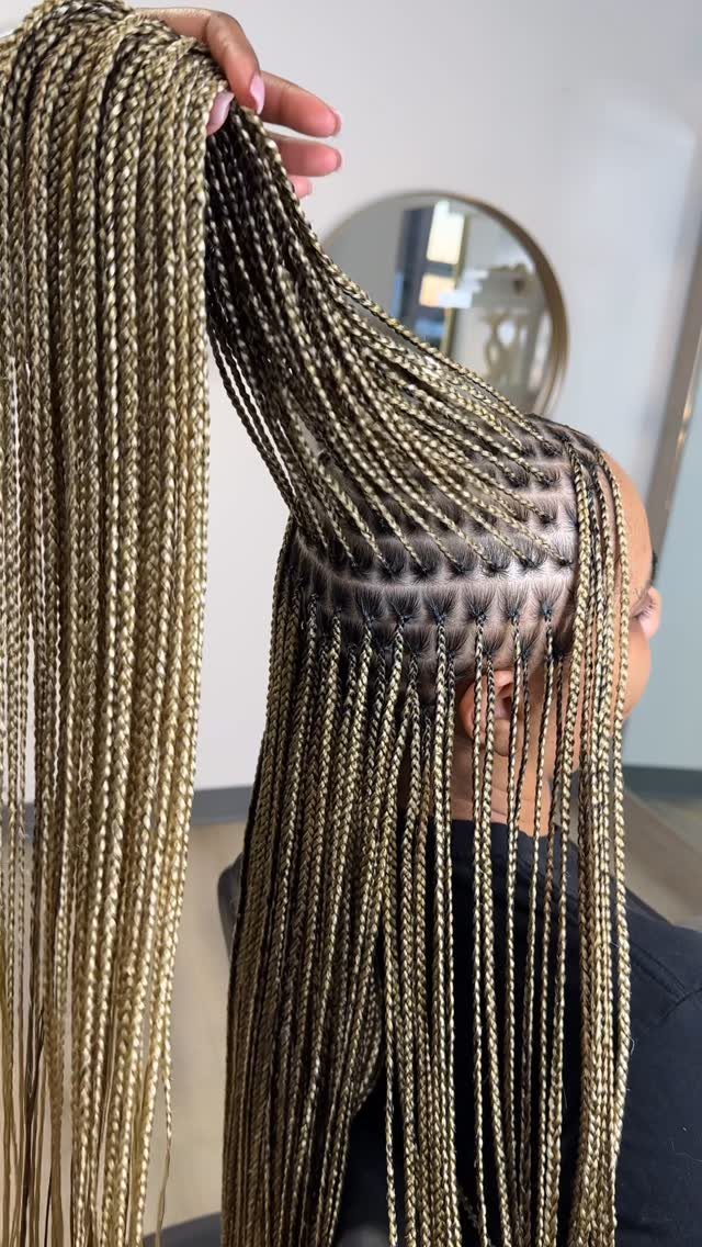 Long blonde and brown knotless braids with a section lifted to show roots.