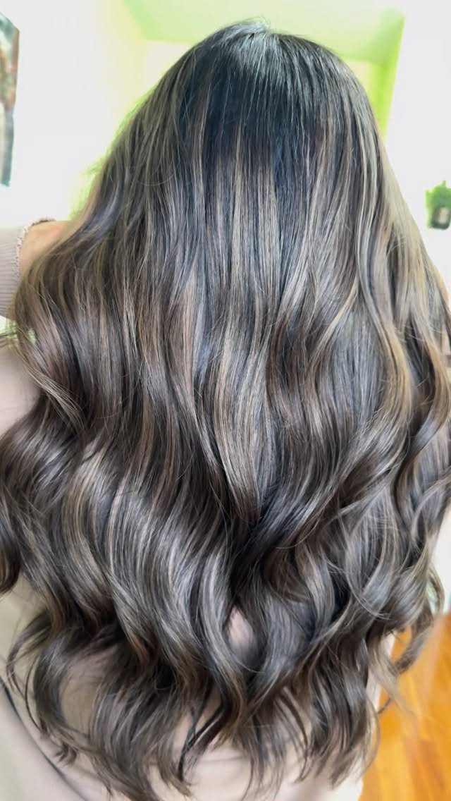 Long wavy hair with dark brown roots and cool ash blonde balayage highlights.