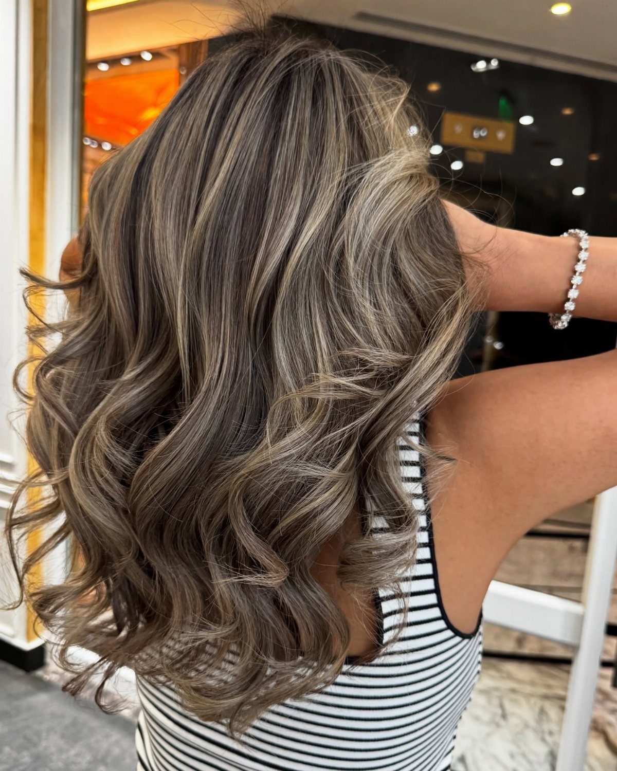 Long wavy hair with dark brown roots and cool-toned ash brown balayage highlights.