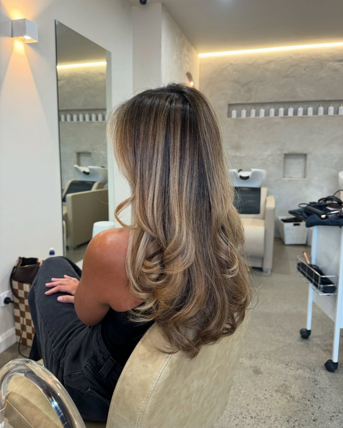 Woman with long wavy dark brown hair and golden blonde balayage highlights in salon