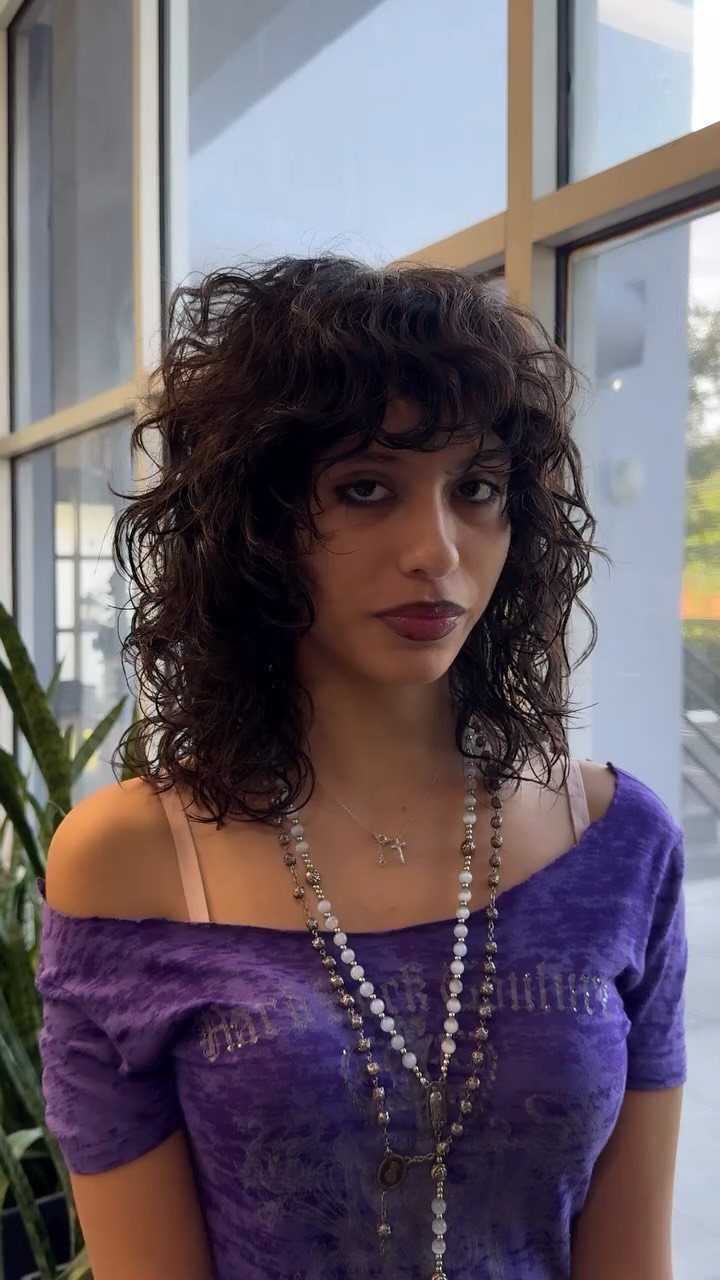 Woman with curly medium length shag haircut and bangs wearing a purple top