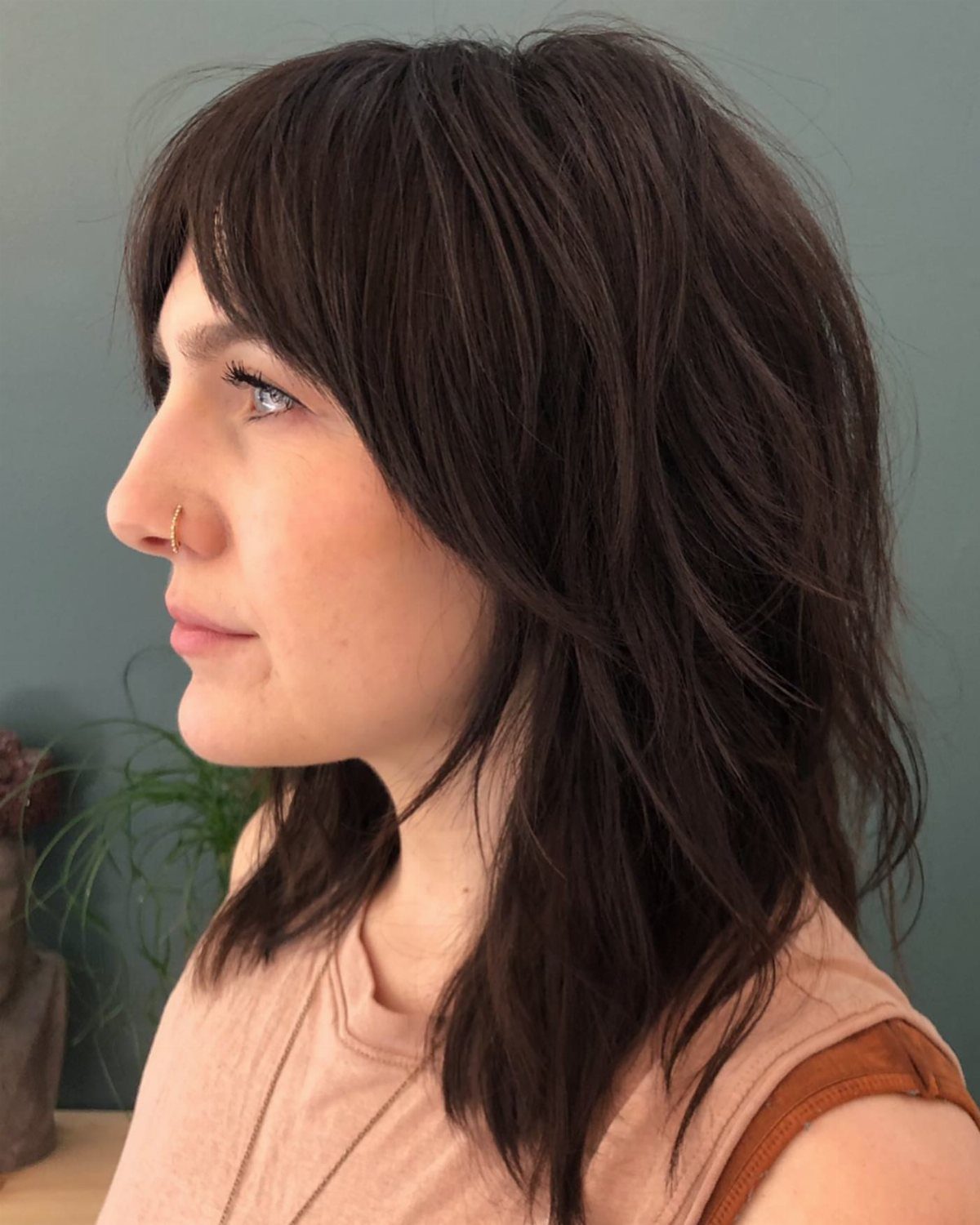 Woman with dark brown medium length shag haircut featuring thick layers and bangs.