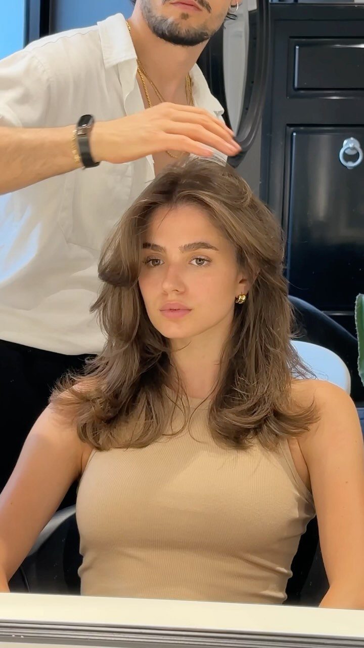 Woman with layered medium length brown hair being styled in a salon