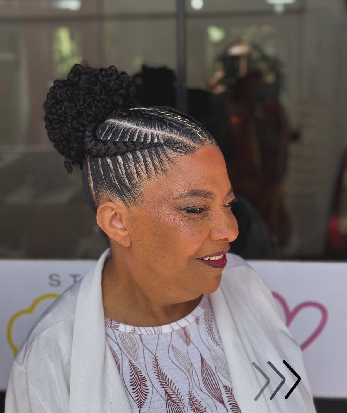 Mature woman with dark hair styled in cornrows and a braided bun updo.