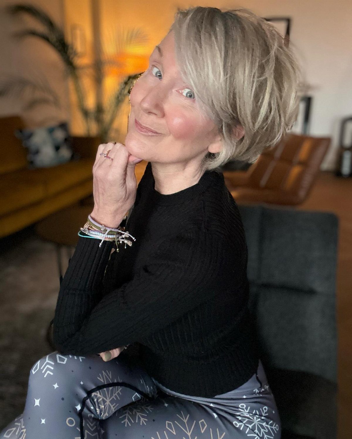 Older woman with a blonde choppy bob hairstyle smiling in a living room