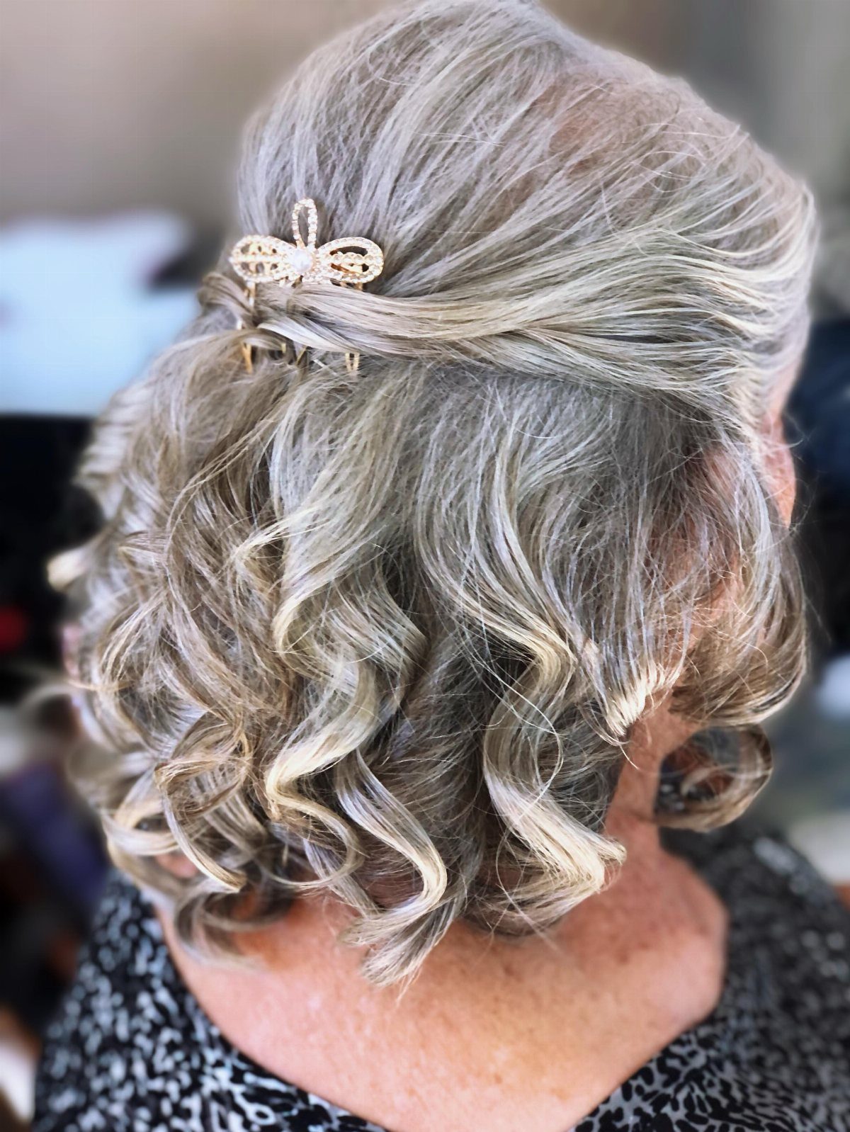 Grey curly hair styled in a half-up hairstyle secured with a gold clip.