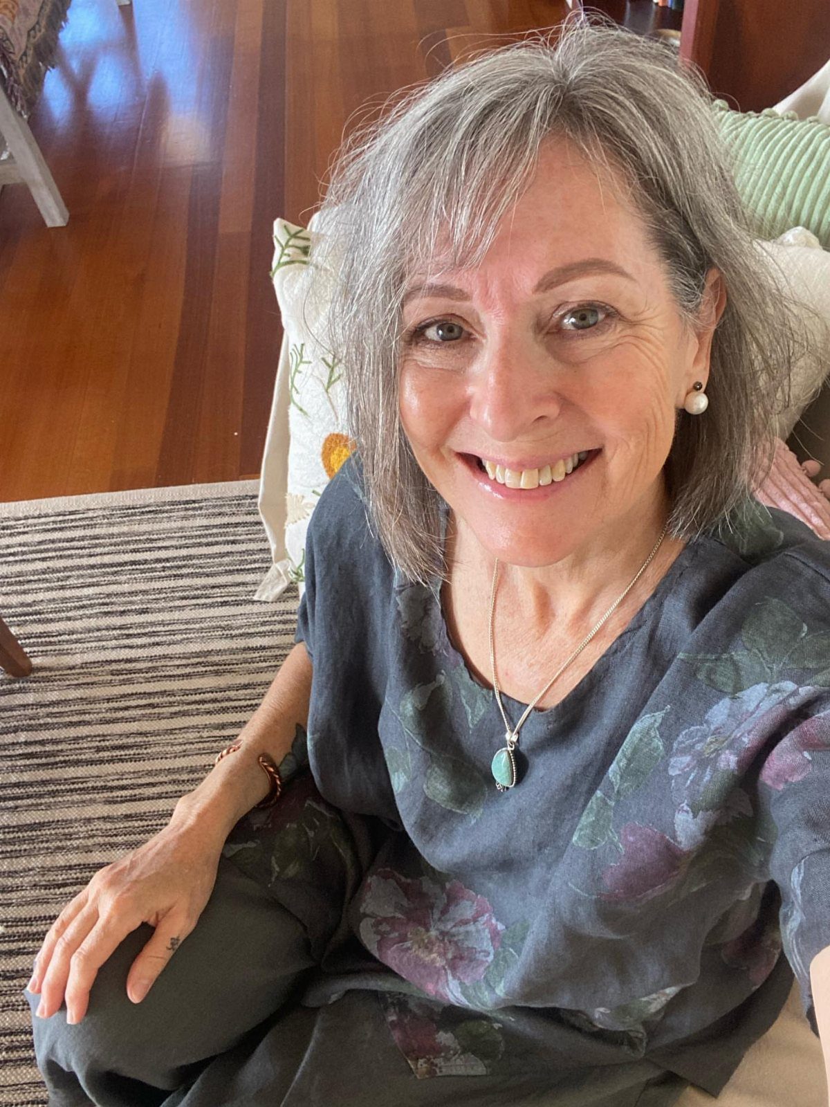 Older woman with a grey long bob hairstyle and bangs smiling indoors.