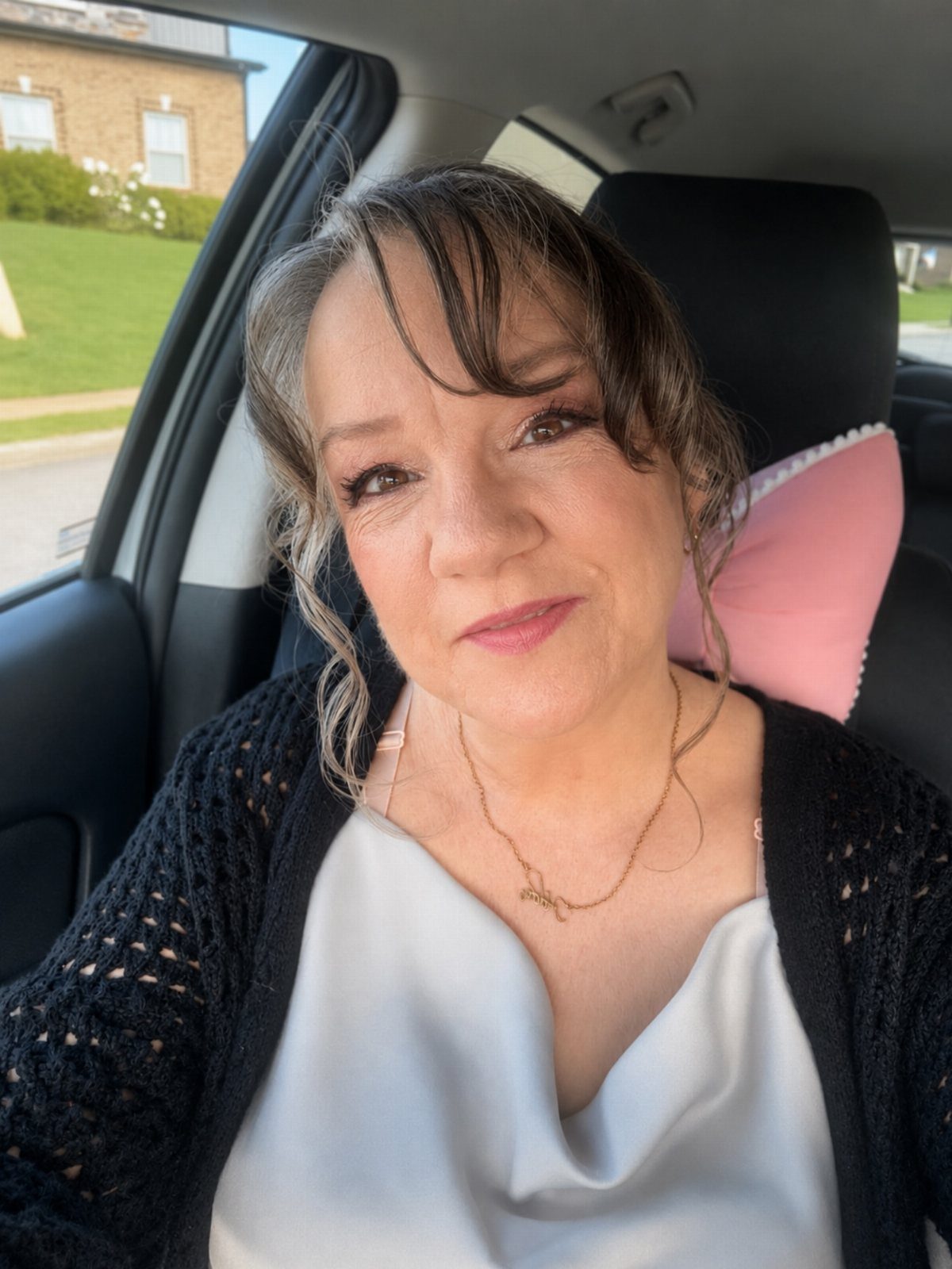 Middle-aged woman with grey-streaked brown hair and bangs sitting in a car.