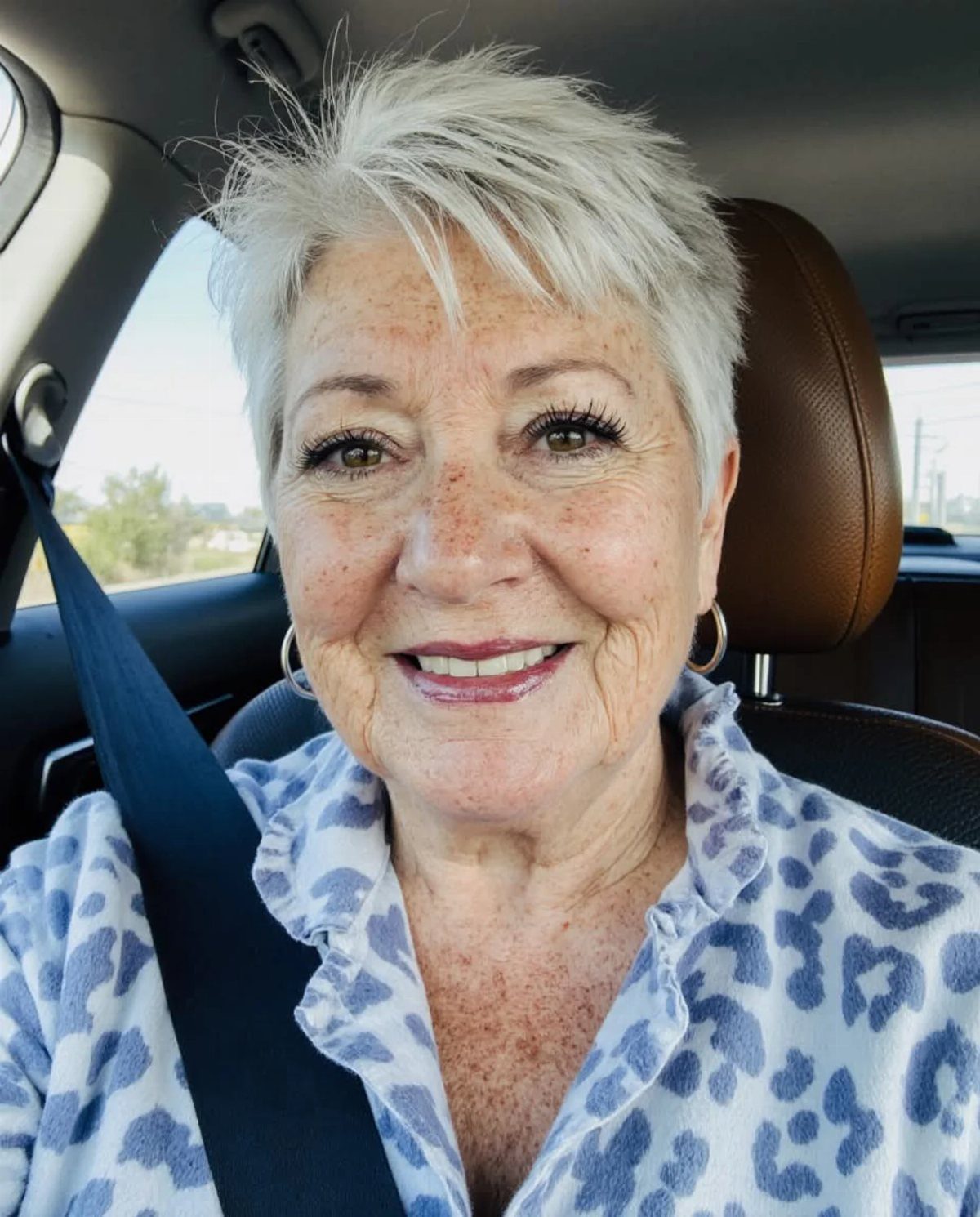 Older woman with short spiky white hair smiling inside a car