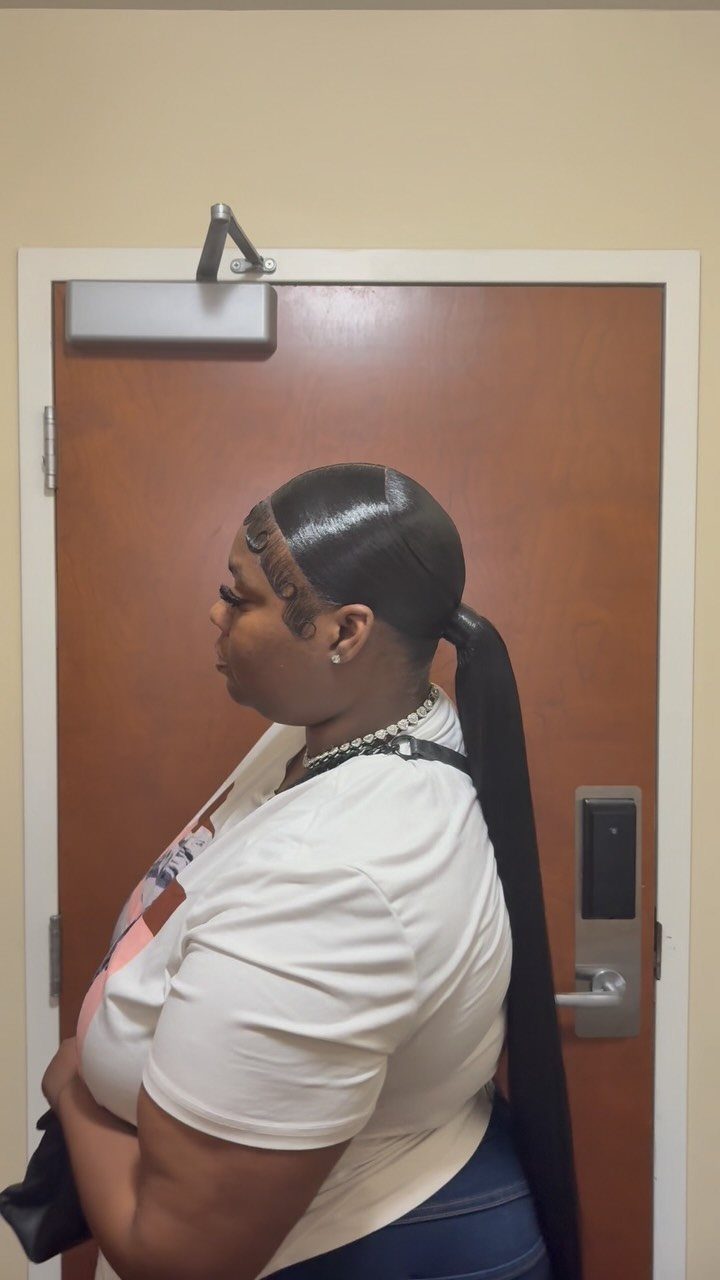 Woman with a sleek, slicked-back ponytail and styled edges standing by a door.