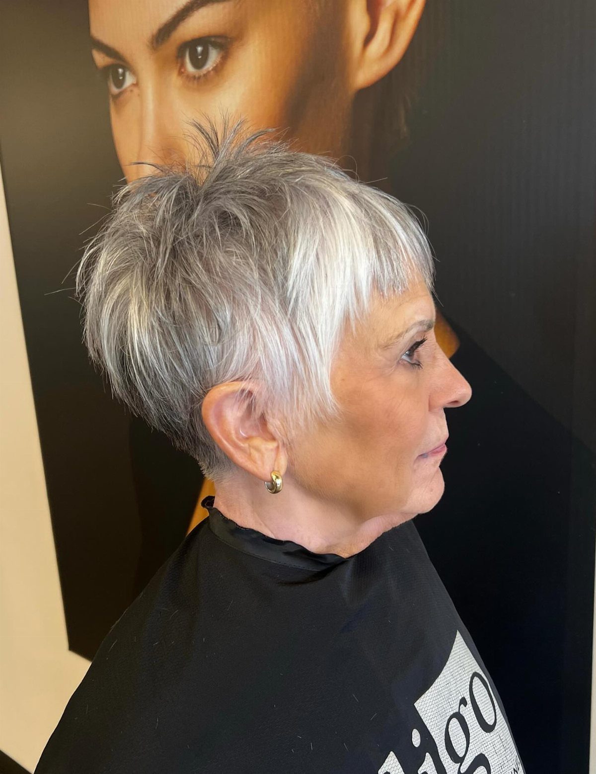 Older woman with a voluminous grey pixie cut in a hair salon setting.